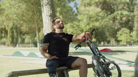 Hombre-Cansado-Con-Pierna-Artificial-Sentado-En-Un-Banco-Después-De-Andar-En-Bicicleta